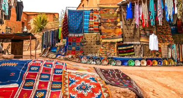 Handwoven colorful Moroccan Berber rugs and textiles displayed at a traditional outdoor market in Morocco.