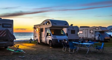 Motorhomes and camper vans parked at a scenic beach campsite during a vibrant coastal sunset.