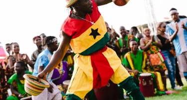 A male dancer performs a traditional Ghanaian dance wearing the Ghana flag colors and straw hats.