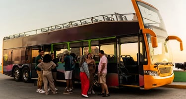 Diverse group of tourists talking next to an open-top double-decker sightseeing bus at sunset.