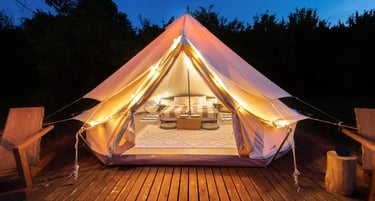 Luxury glamping bell tent at night with warm fairy lights, a cozy bed, and wooden deck.