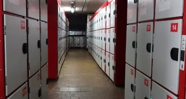 Rows of numbered grey and red storage lockers in a secure basement facility or gym locker room.