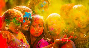 A group of women celebrating the Holi festival with colorful powder and bright yellow light.