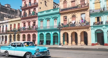 A blue and white classic vintage car drives past colorful colonial buildings in Old Havana, Cuba.