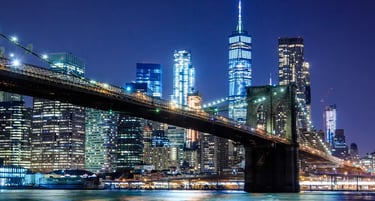 Night view of the Brooklyn Bridge with the illuminated Lower Manhattan skyline and One World Trade Center.