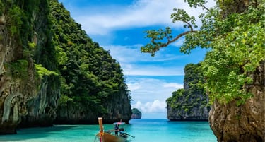 A traditional Thai longtail boat floats on turquoise water by a white sand beach in Phi Phi Islands.
