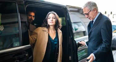 Professional chauffeur holding a car door open for a businesswoman exiting a luxury black SUV.