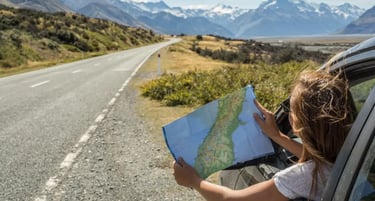 A woman looks at a road map from a car window on a scenic road trip through mountain landscapes.