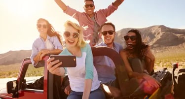 Diverse group of happy friends taking a selfie on a desert road trip in a red convertible.