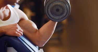 A muscular man performing a bicep curl with a heavy dumbbell at a gym during a strength training workout.
