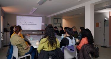 mixed group of people sitting round a table looking at a slide show, with backs to the camera