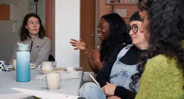 A diverse group of women sitting round a table during a co-learning event, smiling and talking