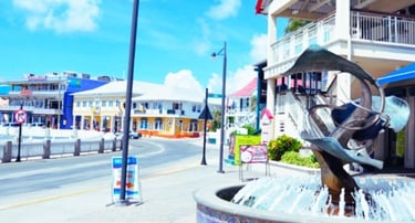 Rua de lojas e galerias em George Town, Ilhas Cayman, com fachadas coloridas e movimento de turistas.