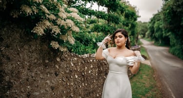 Bride in white dress posing by a stone wall with lush greenery, photographed in Kent.