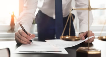 Person Signing Document in front of Scales of Justice