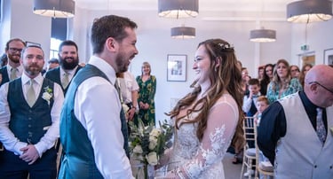 A happy bride and groom laughing during their indoor wedding ceremony surrounded by guests.