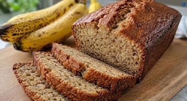 A banana bread loaf on a wooden cutting board, with ripe bananas providing the fruit.