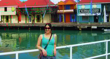 Autora no porto de Antigua. Casinhas coloridas ao fundo.