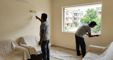 Professional painters applying fresh beige paint to living room walls with a roller and brush.