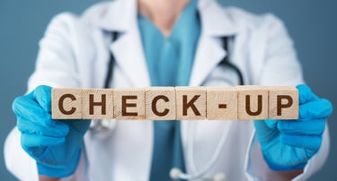 A doctor in a white lab coat holds wooden blocks spelling check-up for a medical exam.