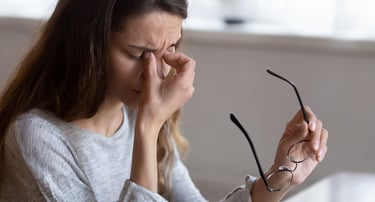 Tired woman holding glasses and rubbing eyes to relieve digital eye strain and headache.
