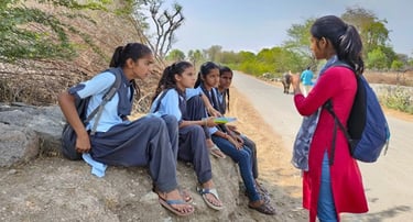 Ambassador Pooja talking to four girls seated on rock.
