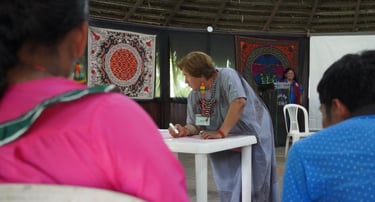 Indigenous woman writing at a community workshop featuring traditional textiles and cultural art.