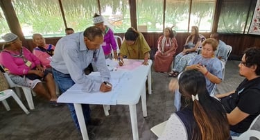 Indigenous community leaders participate in a collaborative workshop, signing documents on a table during a meeting.