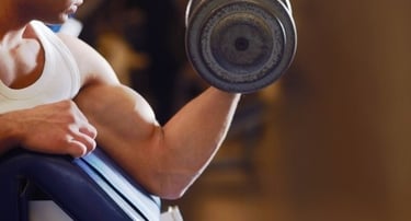 A muscular man performing a bicep curl with a heavy dumbbell at a gym during a strength training workout.