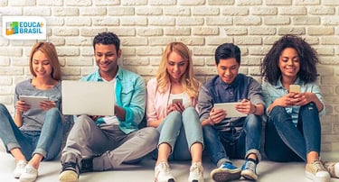 imagem retrata um grupo de estudantes mexendo em seus celulares e computadores