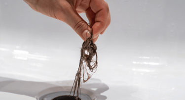 Main retirant des cheveux bouchant un drain de lavabo. Karukera Plomberie intervient pour le débouch