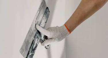 préparation des surfaces : un peintre tenant un couteau ratisse un mur avec une truelle