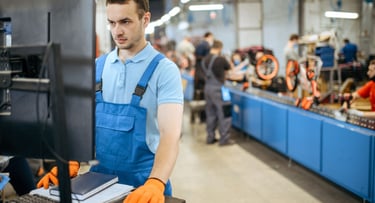 A factory worker in blue overalls using a computer at a bicycle manufacturing assembly line.