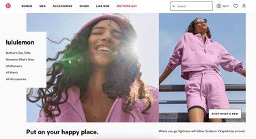 A woman with brown curly hair, smiling, wearing a pink hoodie, with the sun flaring behind her.