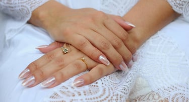 Close-up das mãos de uma noiva com manicure francesa em esmalte cromado branco e anéis de ouro,.