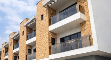 Modern multi-story townhouse complex with tan stone siding, glass balconies, and gray exterior walls.
