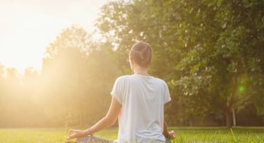 A woman practicing outdoor yoga and meditation in a sunny green park during sunset.