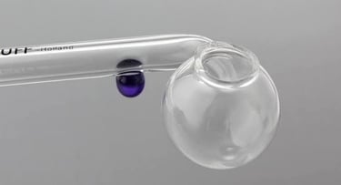 A clear glass vaporizer oil pipe with a round bulb bowl and a blue marble accent on a gray background.