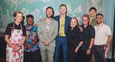 A group of chefs and BQFF founders standing in front of a wall with a wall with a mural