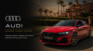 Red Audi RS3 luxury sedan for rent parked at a tropical resort with palm trees at sunset.