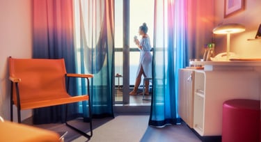 A traveler drinking coffee on a cruise ship balcony with colorful ombre curtains and modern cabin decor.