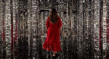 Woman in a flowing red dress walking through an immersive infinity mirror room with glowing fairy lights.