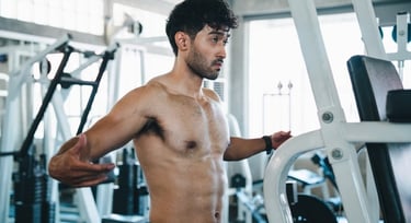 Shirtless athletic man performing chest exercises on a gym fly machine for bodybuilding.