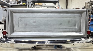 Rear view of a classic vintage truck undergoing metal restoration with a chrome bumper.