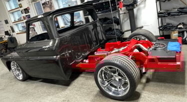Custom black classic pickup truck restoration featuring a bright red chassis and chrome wheels in a garage.
