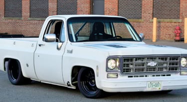 Custom white classic Chevrolet C10 pickup truck with lowered suspension and black wheels parked by a brick building.