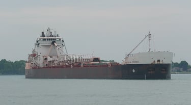 A black and white lake freighter approaching, viewed from the front right.