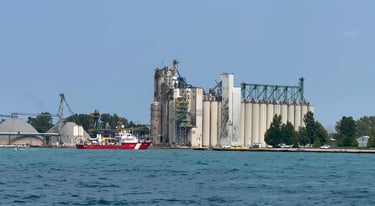 Red and white Canadian Coast Guard vessel Limnos passing grain silos, arriving in Sarnia Harbor.