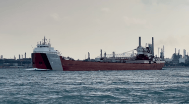 Classic forward pilothouse lake freighter Philip R. Clarke passing an oil refinery.