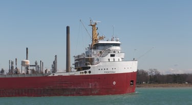 Close-up of Frontenac's red and white forward pilothouse passing an oil refinery.